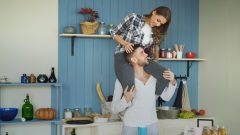 Happy young couple having fun in kitchen at home. Girl is sitting on boyfriend's neck and embrace him