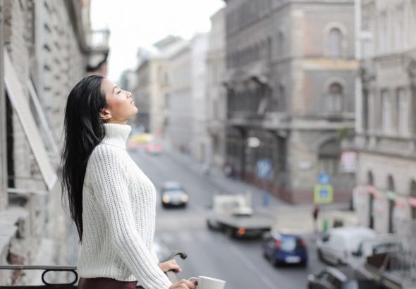 Woman enjoying a moment of relaxation on a balcony overlooking a city street.