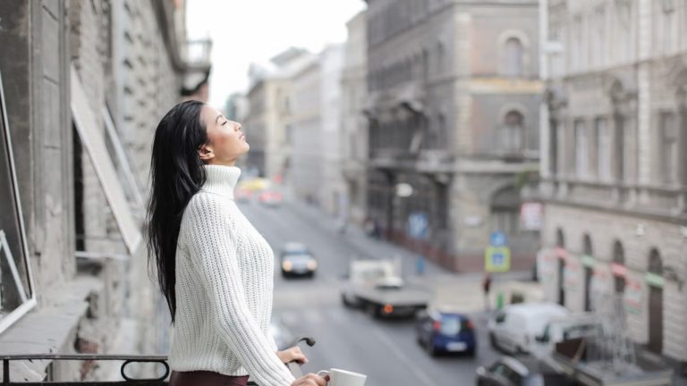 Woman enjoying a moment of relaxation on a balcony overlooking a city street.
