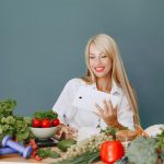 Woman using a tablet surrounded by fresh vegetables at a table, showcasing healthy lifestyle and technology.