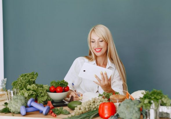 Woman using a tablet surrounded by fresh vegetables at a table, showcasing healthy lifestyle and technology.