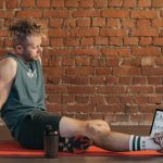 Athletic man sitting and resting on a mat in an urban gym, with a tablet and weights visible.